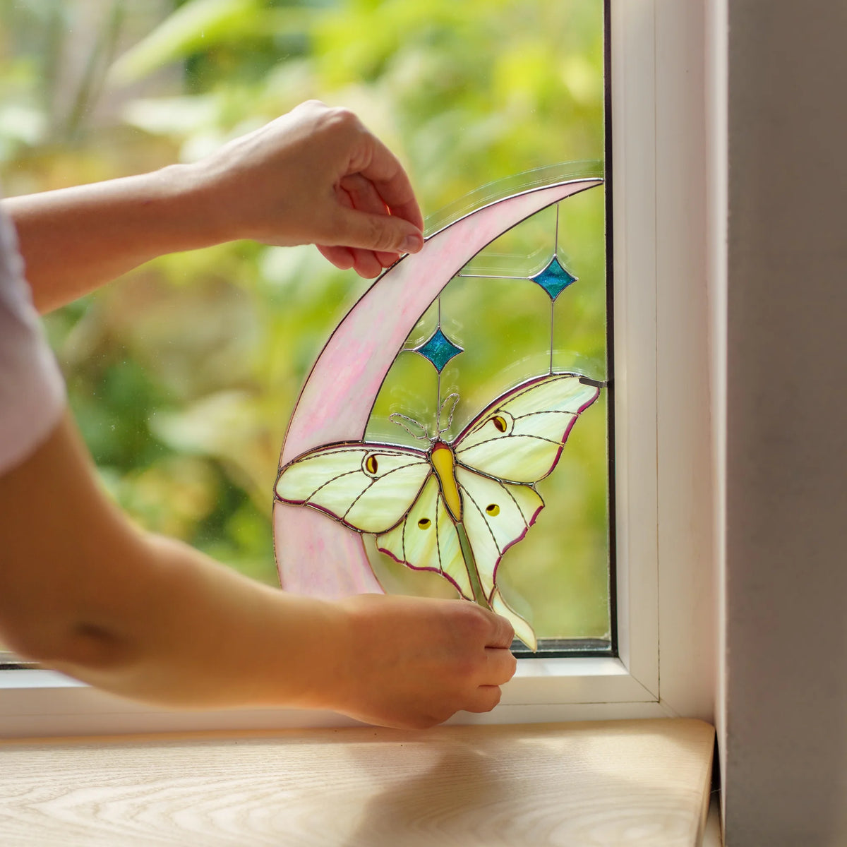 Handmade stained glass luna moth and crescent moon window corner being clipped into a garden window