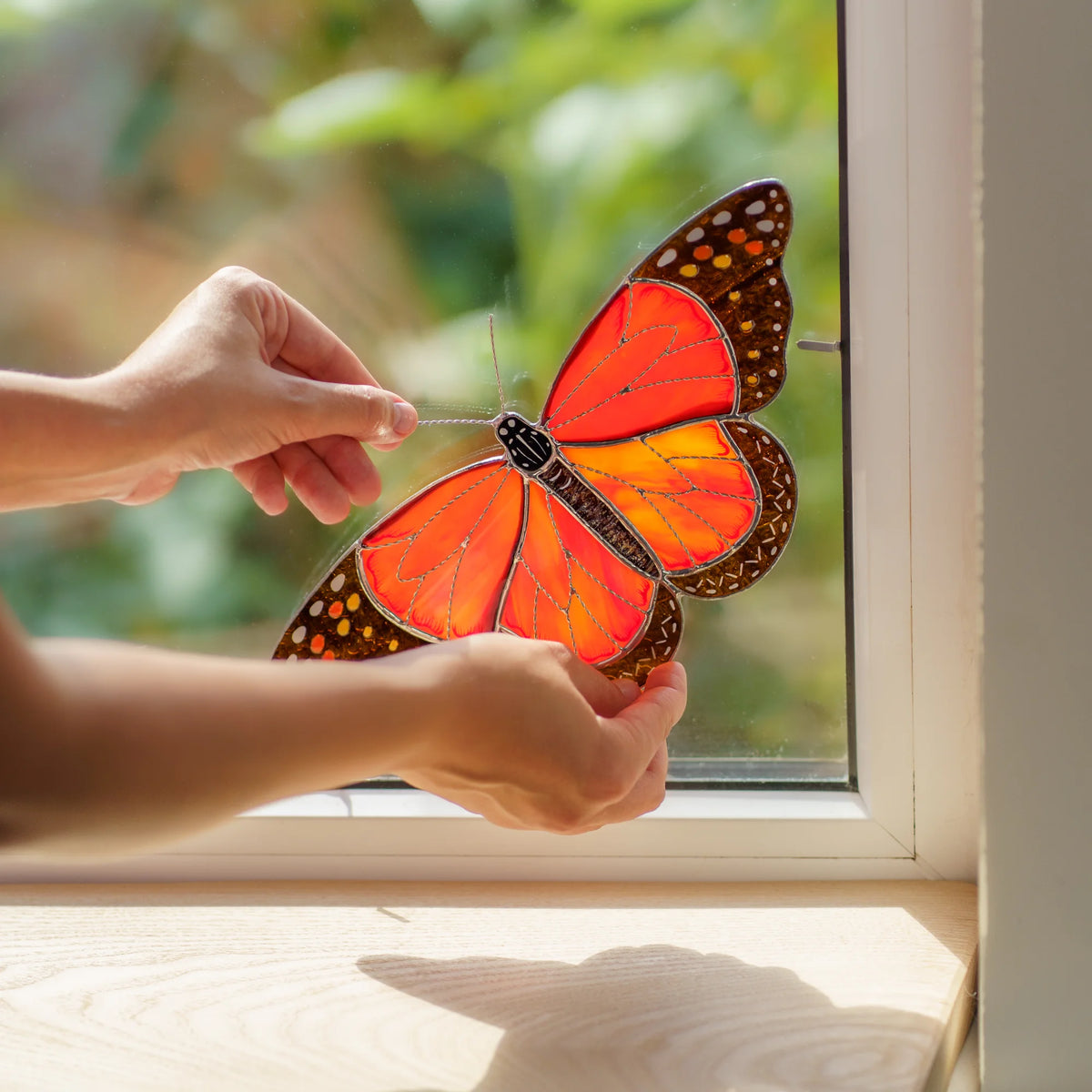 Handmade stained glass monarch butterfly window corner suncatcher being clipped into a sunny window