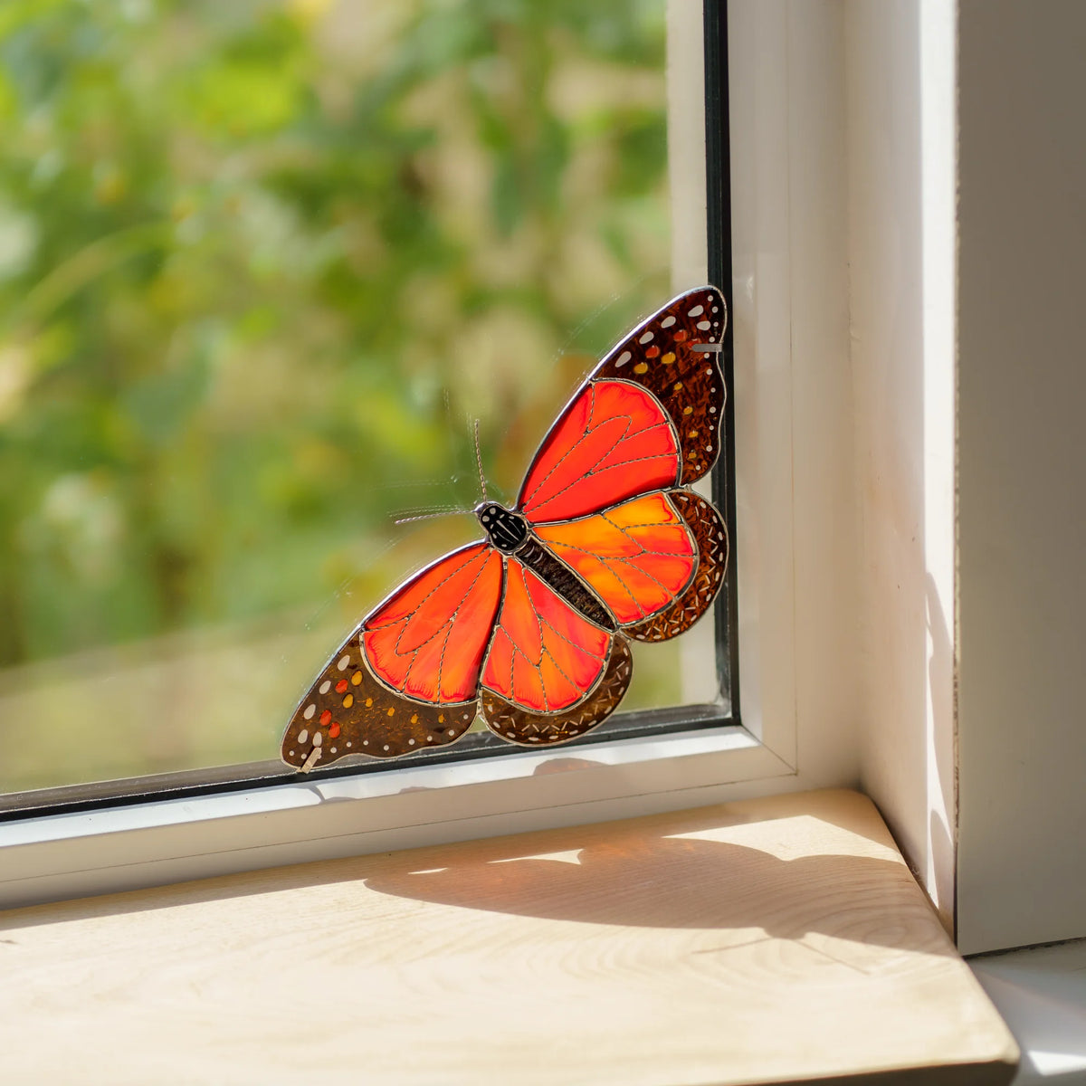 Monarch butterfly glass art settled in the lower corner of a window, its shadow falling across the sill