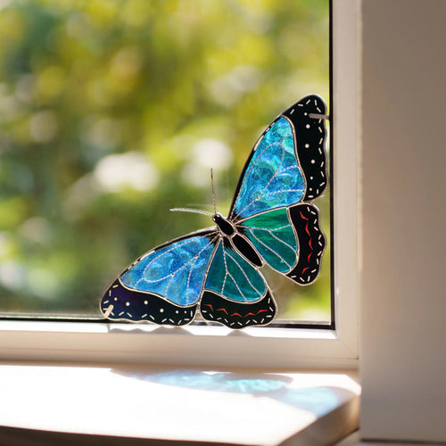 Blue morpho glass butterfly with black dotted borders fitted into a sunny window corner