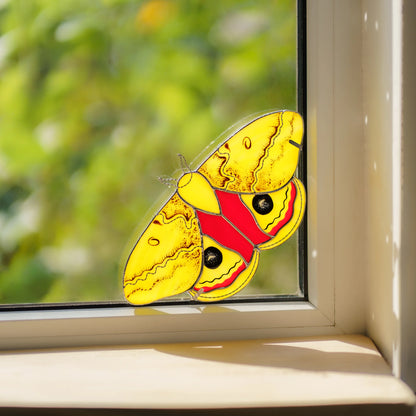 Handmade stained glass io moth window corner suncatcher with black eyespots in a sunny window