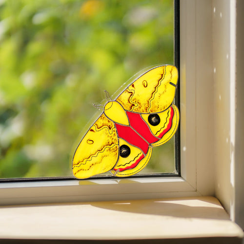 Handmade stained glass io moth window corner suncatcher with black eyespots in a sunny window