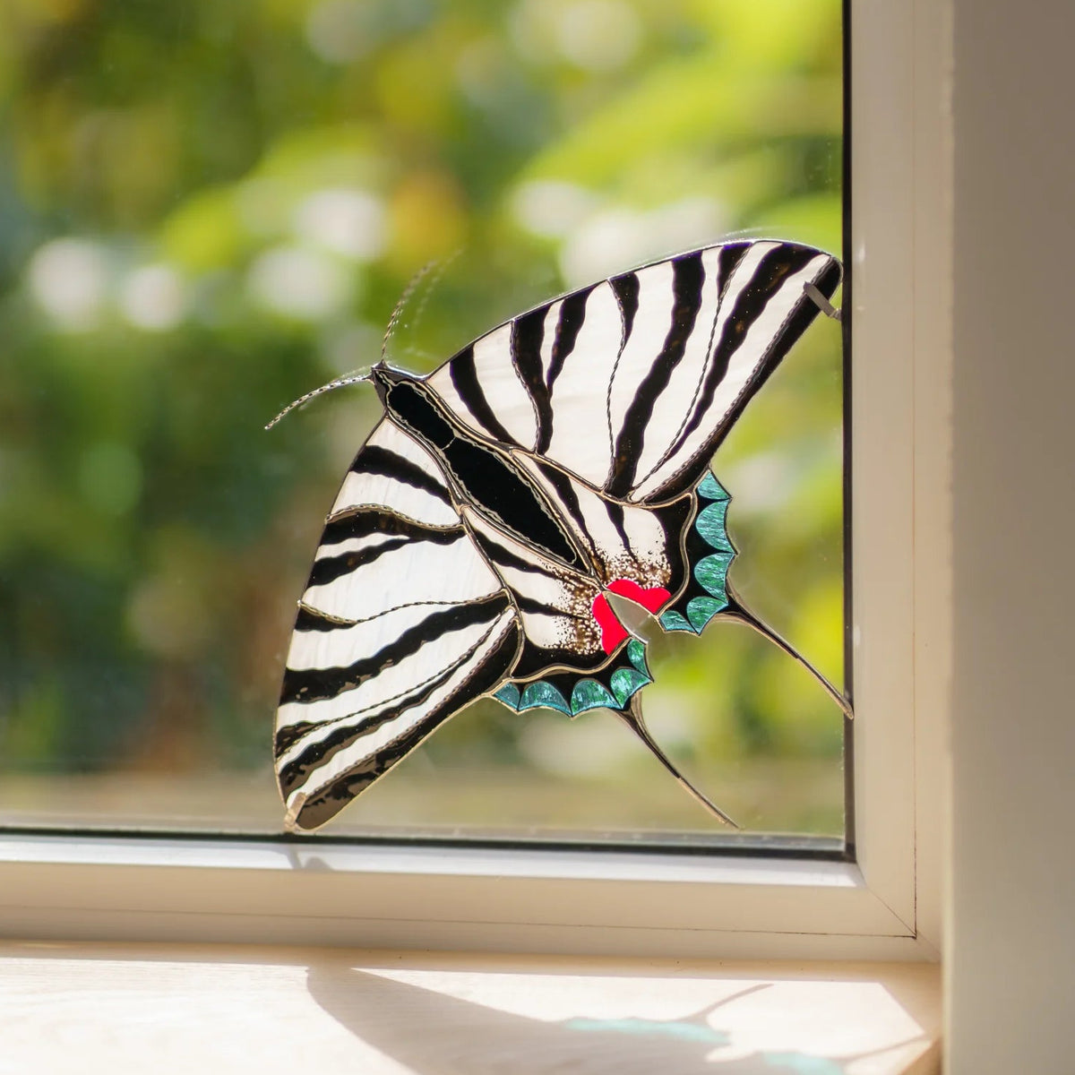 Handmade stained glass zebra swallowtail window corner suncatcher with long tails in a garden-view window