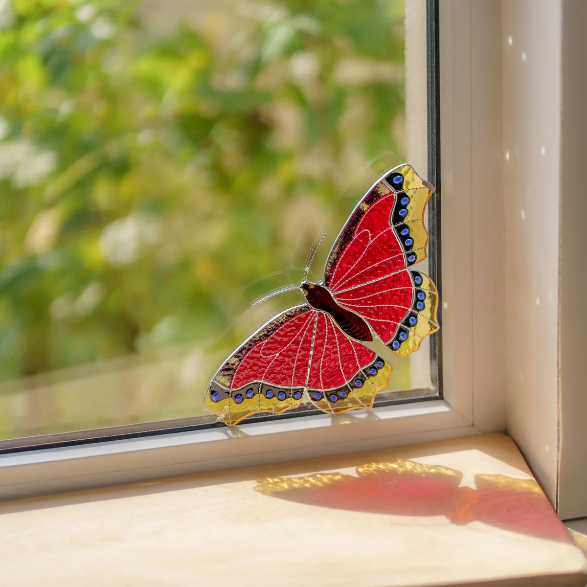 Handmade stained glass mourning cloak butterfly window corner suncatcher casting red light on the sill