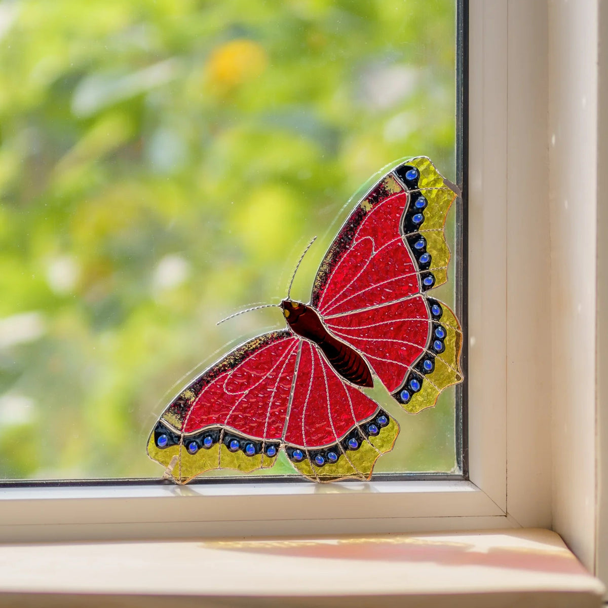 Handmade stained glass mourning cloak butterfly window corner panel casting red light on the sill