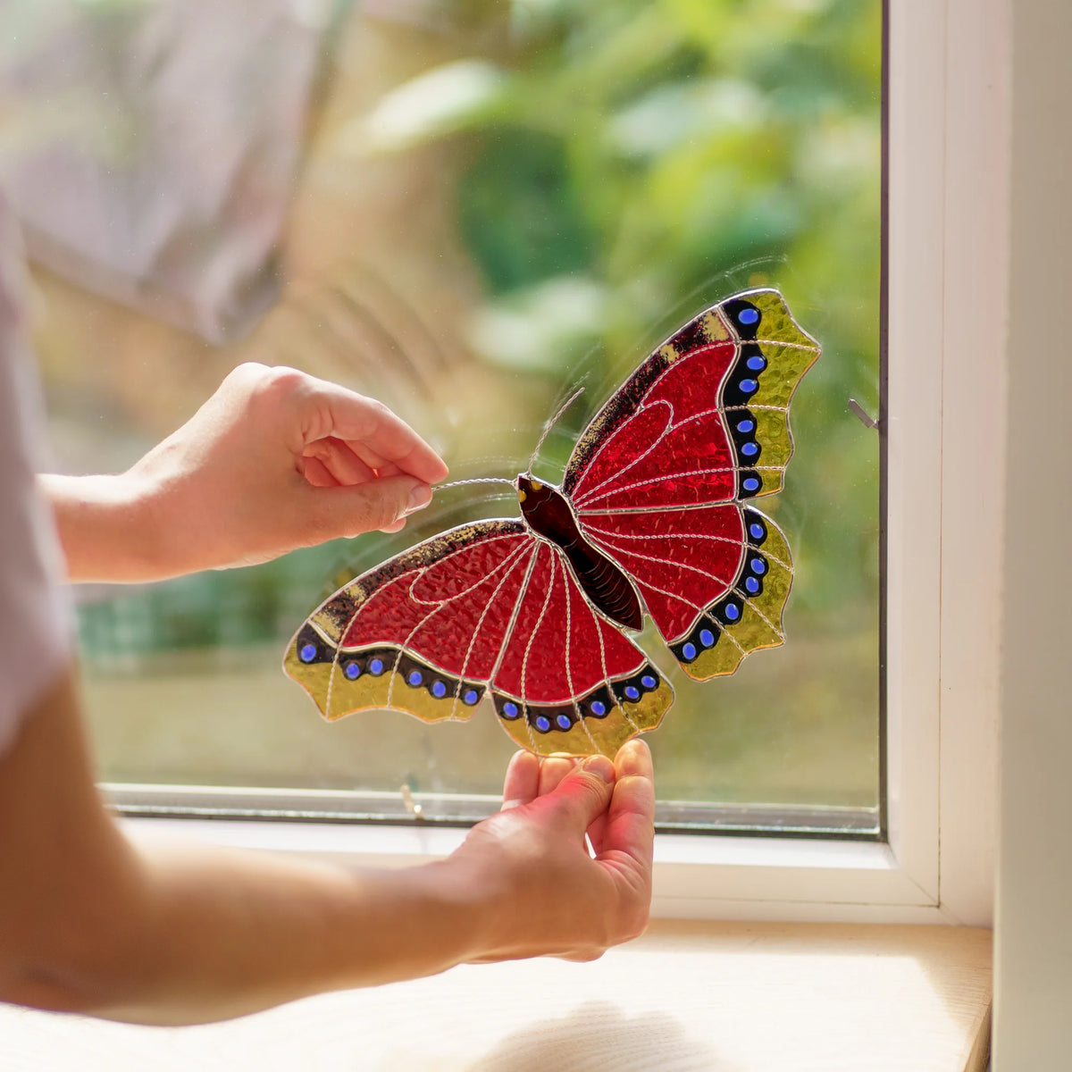 Hands placing the red butterfly into a window corner, a small metal clip visible on the frame