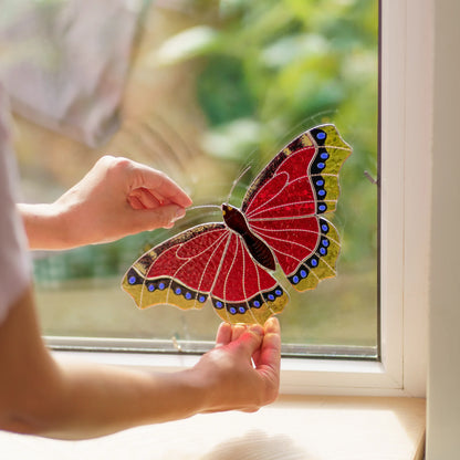 Hands placing the red butterfly into a window corner, a small metal clip visible on the frame