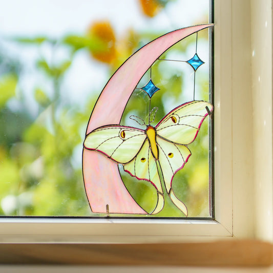 Close view of the luna moth resting on a pink stained glass moon, two blue stars on fine wire above