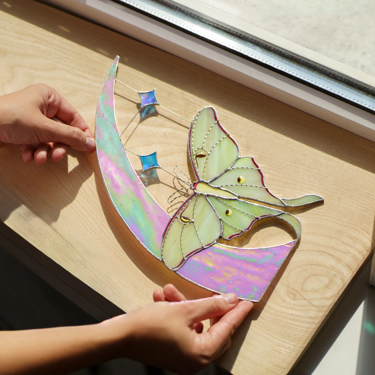 Iridescent pink and green moon with luna moth laid on a sunny wooden sill, stars casting blue light