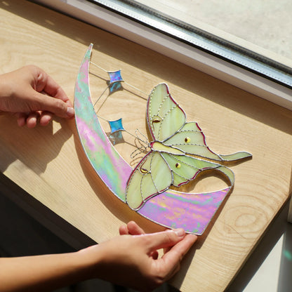 Iridescent pink and green moon with luna moth laid on a sunny wooden sill, stars casting blue light