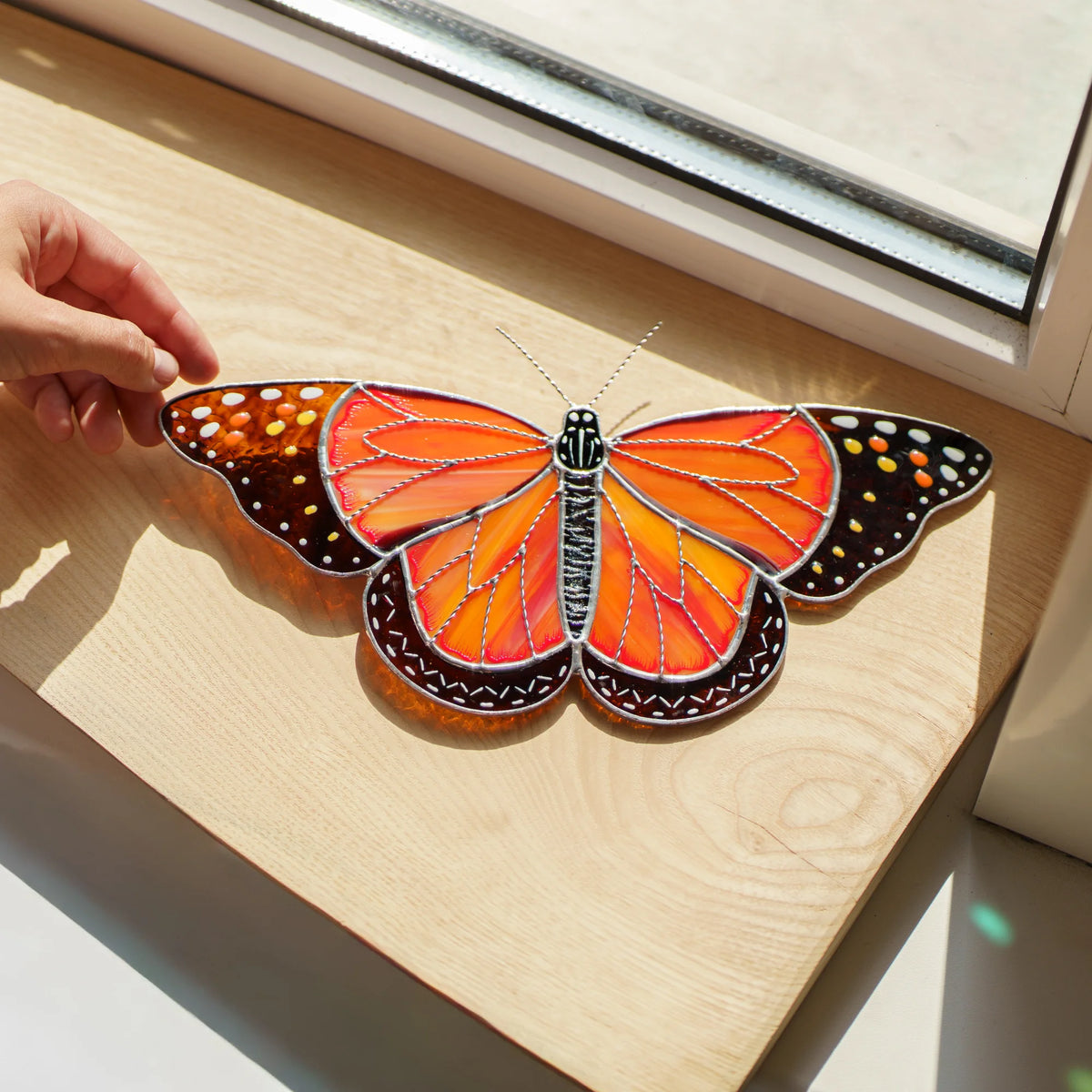 Monarch suncatcher on a sunlit wooden sill, silver-lined veins over streaky orange glass