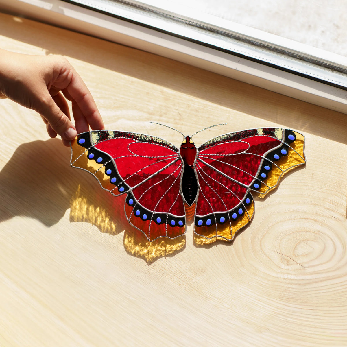 Mourning cloak butterfly glass art on a sunlit wooden sill, its amber edges throwing golden light