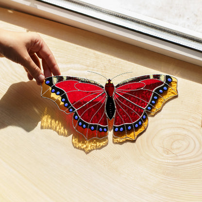 Mourning cloak butterfly glass art on a sunlit wooden sill, its amber edges throwing golden light