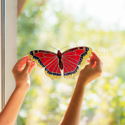 Backlit stained glass butterfly raised against a sunny window, textured crimson glass glowing in daylight