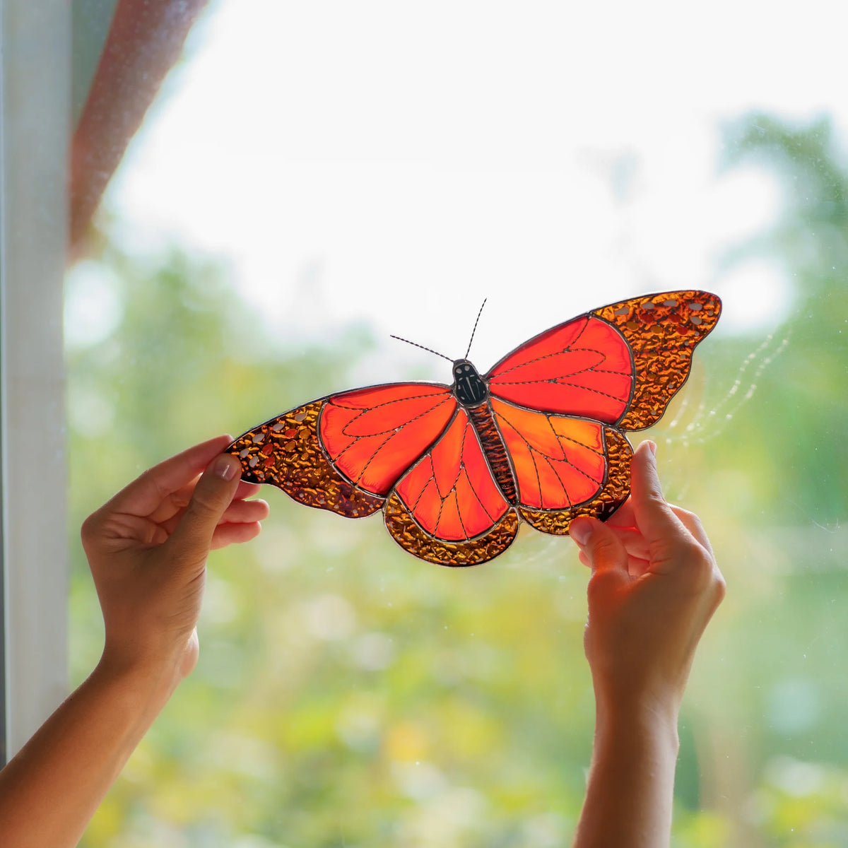 Backlit stained glass monarch glowing orange in daylight, textured amber glass along the wing edges