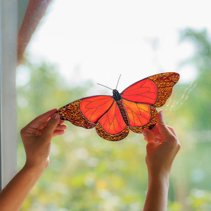 Backlit stained glass monarch glowing orange in daylight, textured amber glass along the wing edges