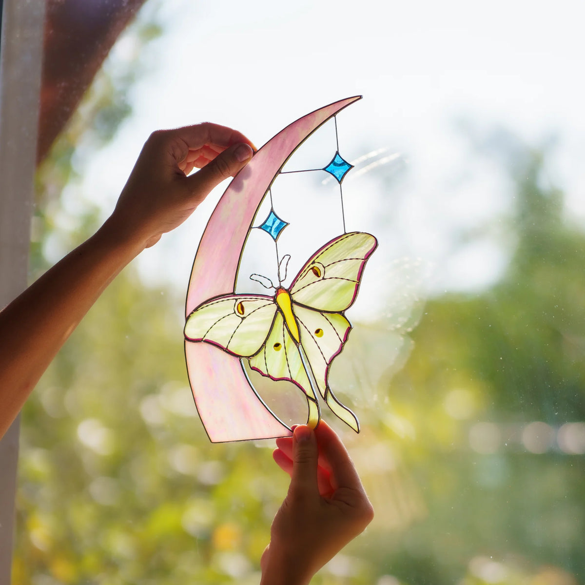 Backlit celestial stained glass with crescent moon, blue stars and pale green luna moth in daylight