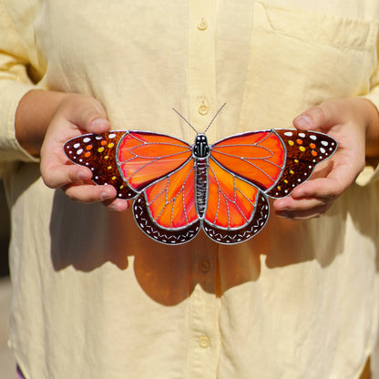 Person in a yellow shirt holding the glass monarch with both hands to show its size and wingspan