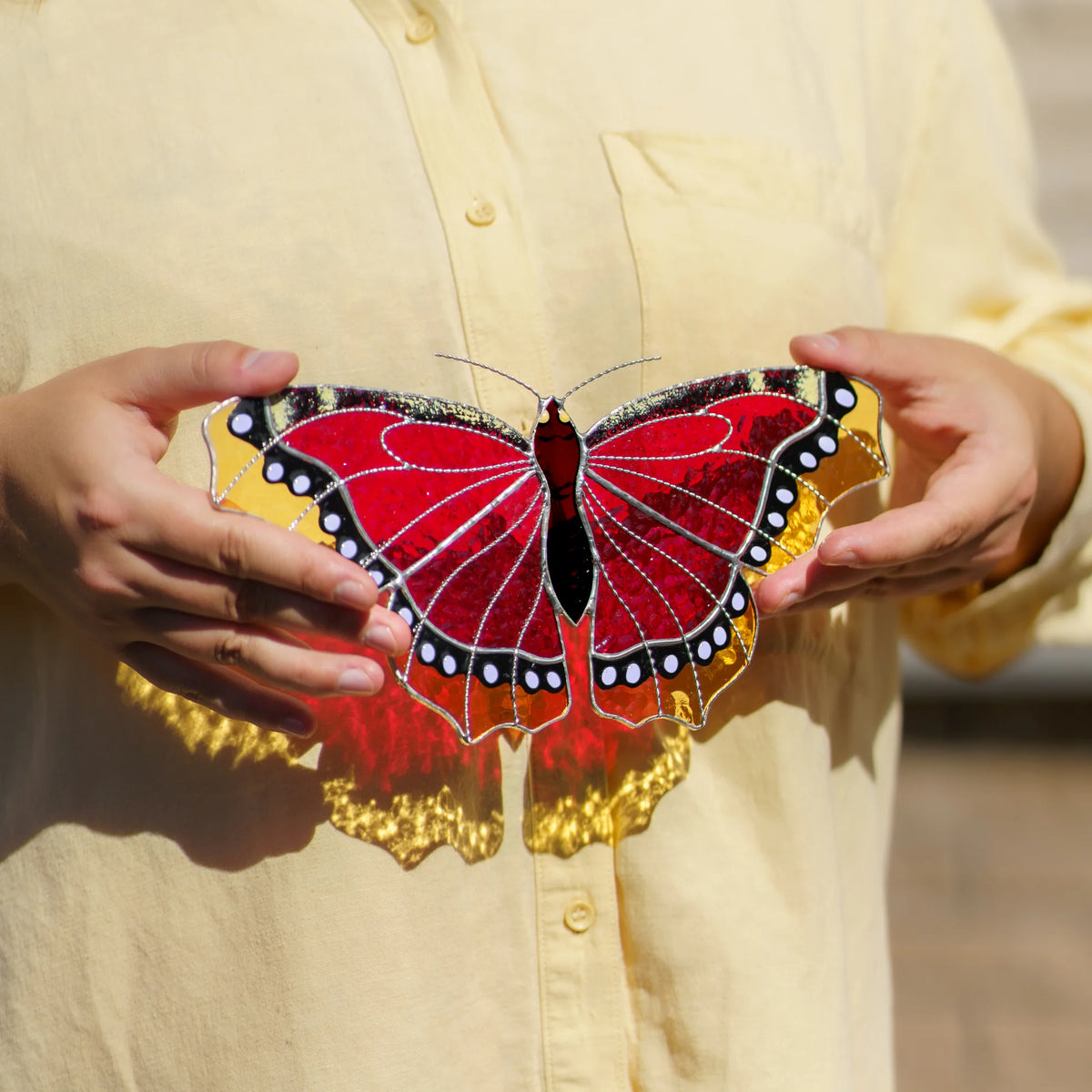 Holding the glass butterfly against a yellow shirt, red and amber light falling through the wings