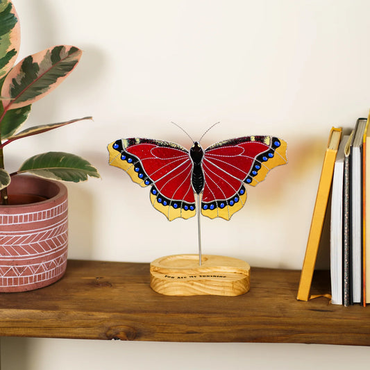 Mourning cloak butterfly stained glass suncatcher on its wooden stand beside potted plants and books
