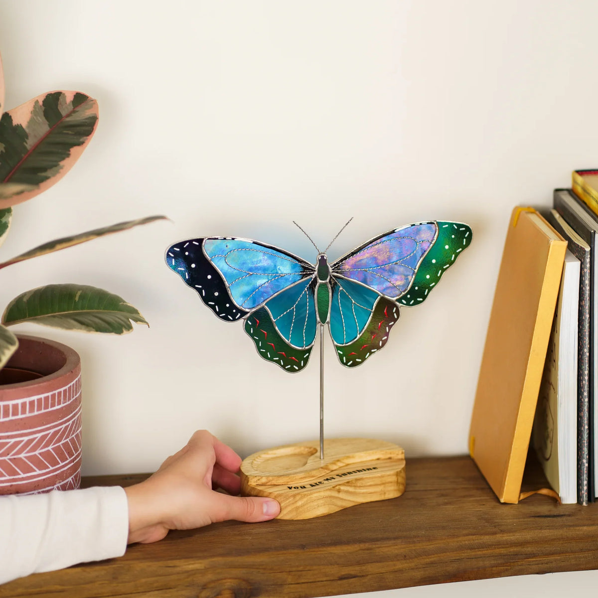 Hand placing the blue morpho butterfly suncatcher's wooden base on a bookshelf