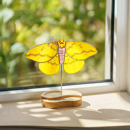 Imperial moth stained glass suncatcher glowing in sunlight on a windowsill