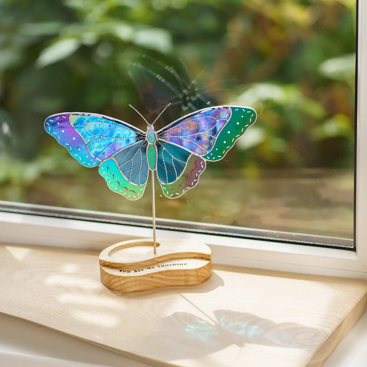 Blue morpho butterfly stained glass suncatcher glowing in sunlight on a windowsill
