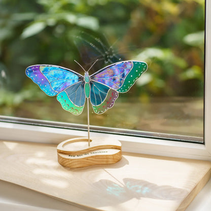 Blue morpho butterfly stained glass suncatcher glowing in sunlight on a windowsill