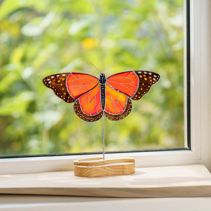Stained glass monarch butterfly suncatcher on a windowsill with a garden view behind it