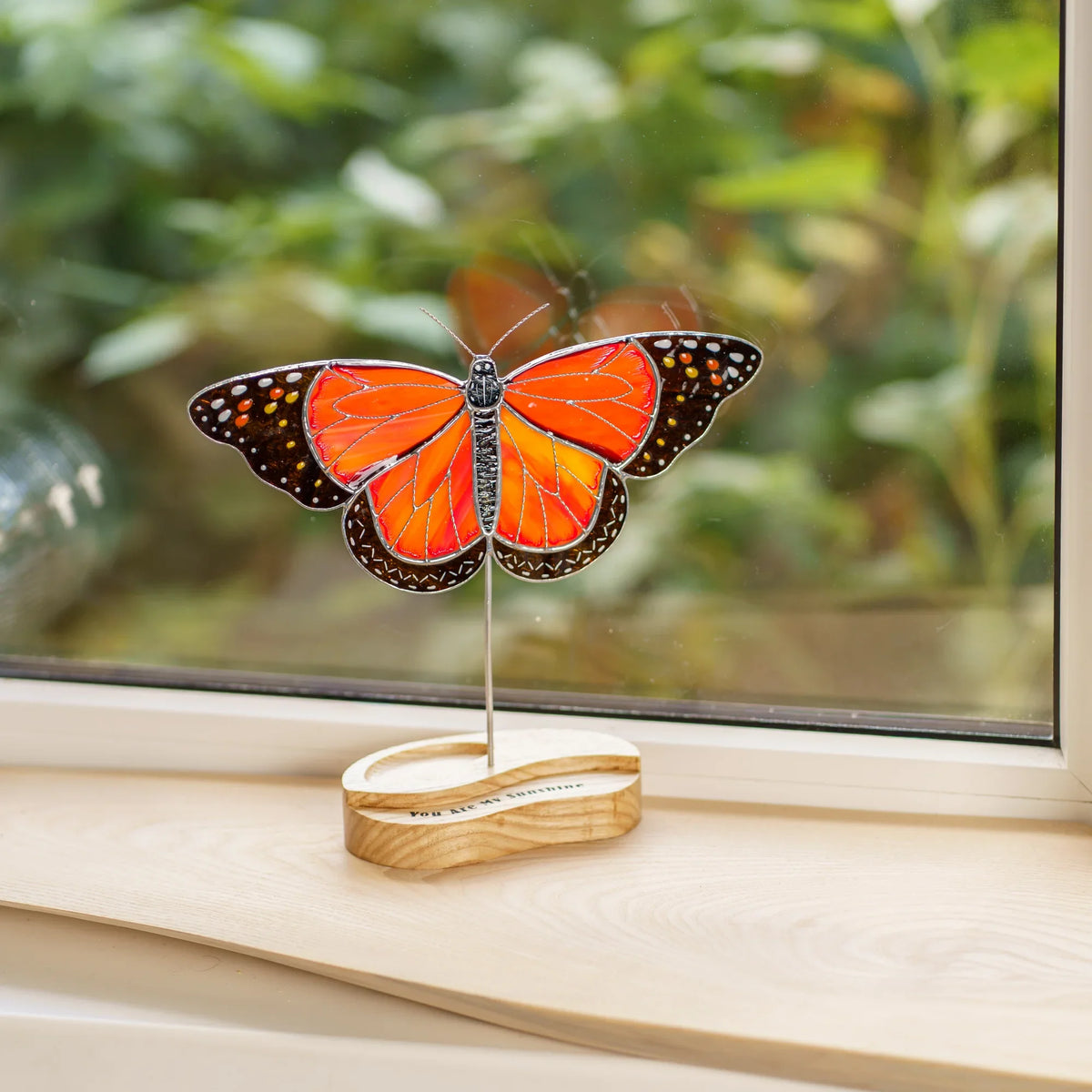 Monarch butterfly stained glass suncatcher on a windowsill, backlit by daylight