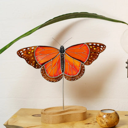 Monarch butterfly stained glass suncatcher on its wooden stand beside a green leaf