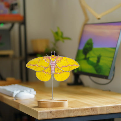 Imperial moth suncatcher on a wooden desk stand next to a keyboard and monitor