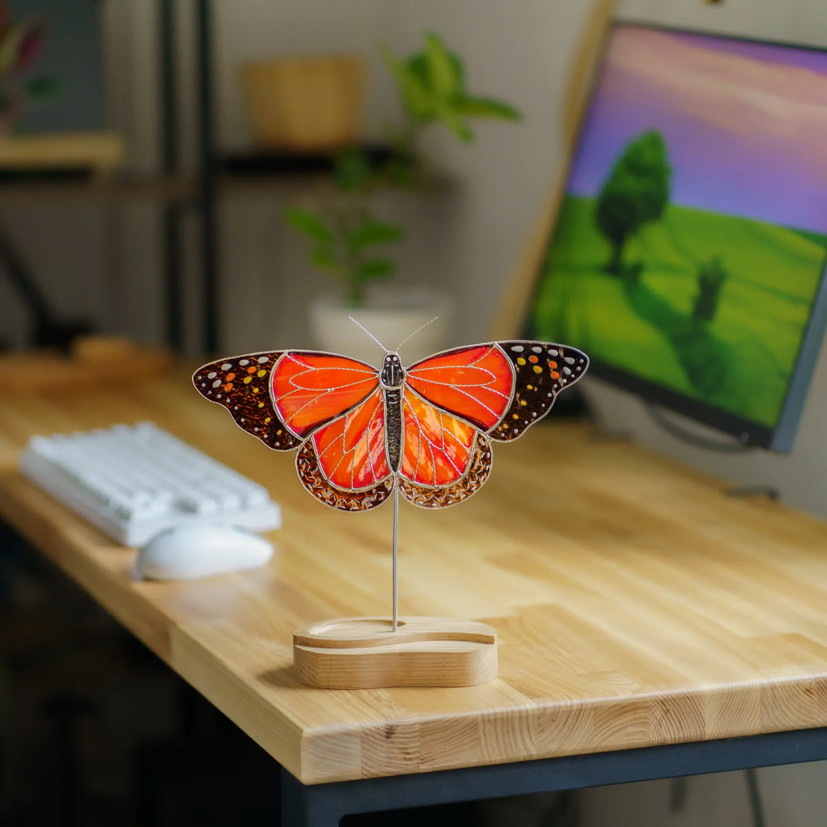 Monarch butterfly suncatcher on a wooden desk stand next to a keyboard and monitor