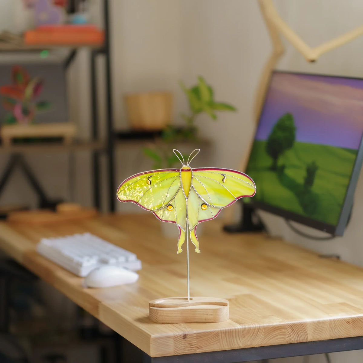 Luna moth suncatcher on a wooden desk stand next to a keyboard and monitor