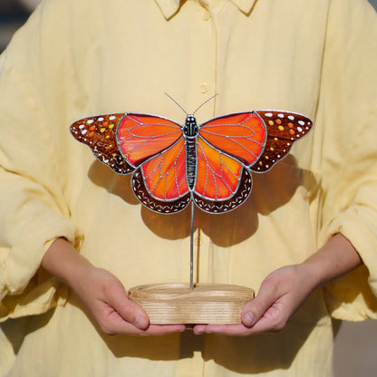 Person holding the monarch butterfly stained glass suncatcher by its engraved wooden base