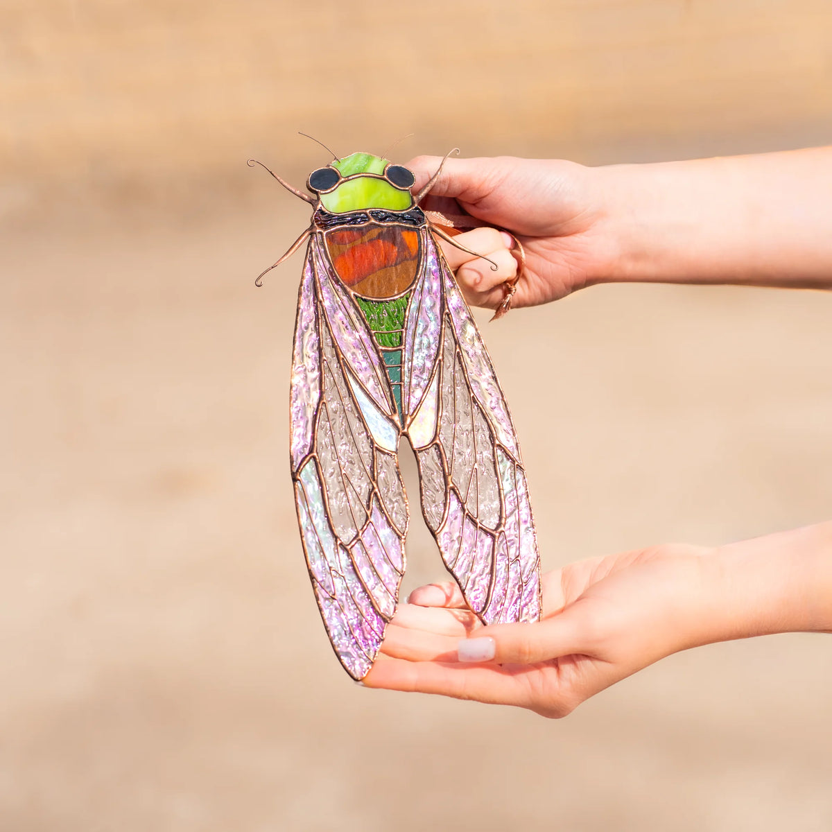 A person holding up a detailed stained glass cicada outdoors, highlighting it as an exquisite and thoughtful gift choice.