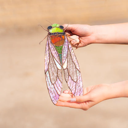 A person holding up a detailed stained glass cicada outdoors, highlighting it as an exquisite and thoughtful gift choice.