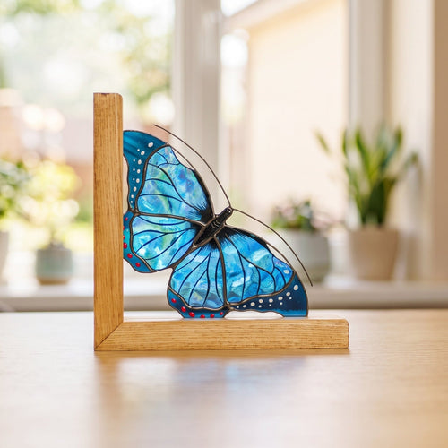 A gorgeous blue stained glass butterfly displayed on a sunny windowsill, highlighting its intricate details, rich textures, and the beautiful light it brings into the space.
