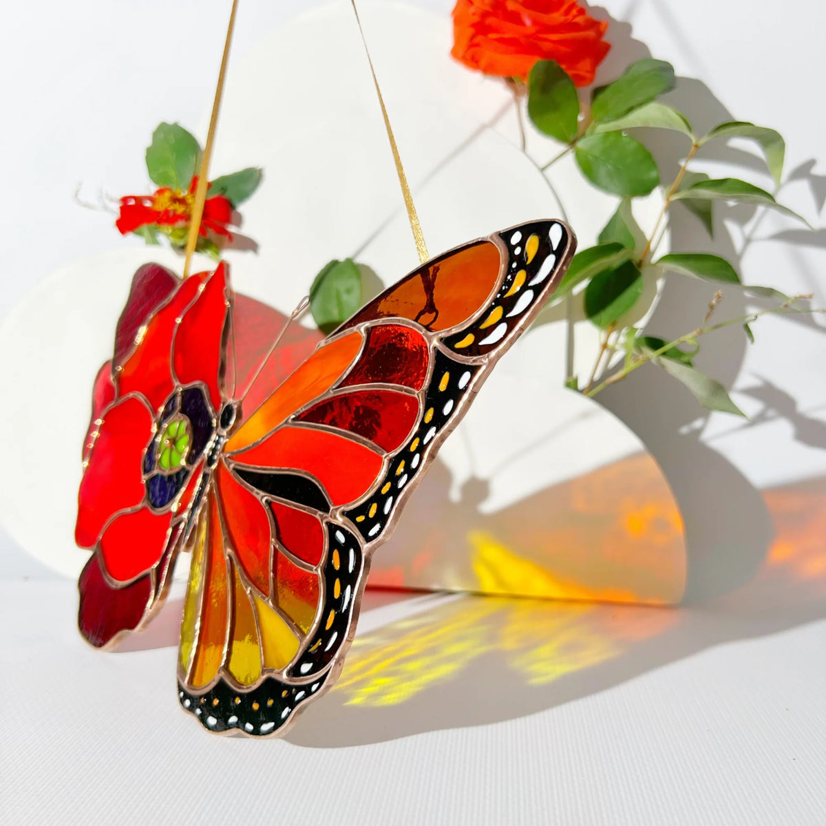 A stunning stained glass butterfly blending a red poppy and a monarch wing, displayed against a white background with floral accents casting colorful light.
