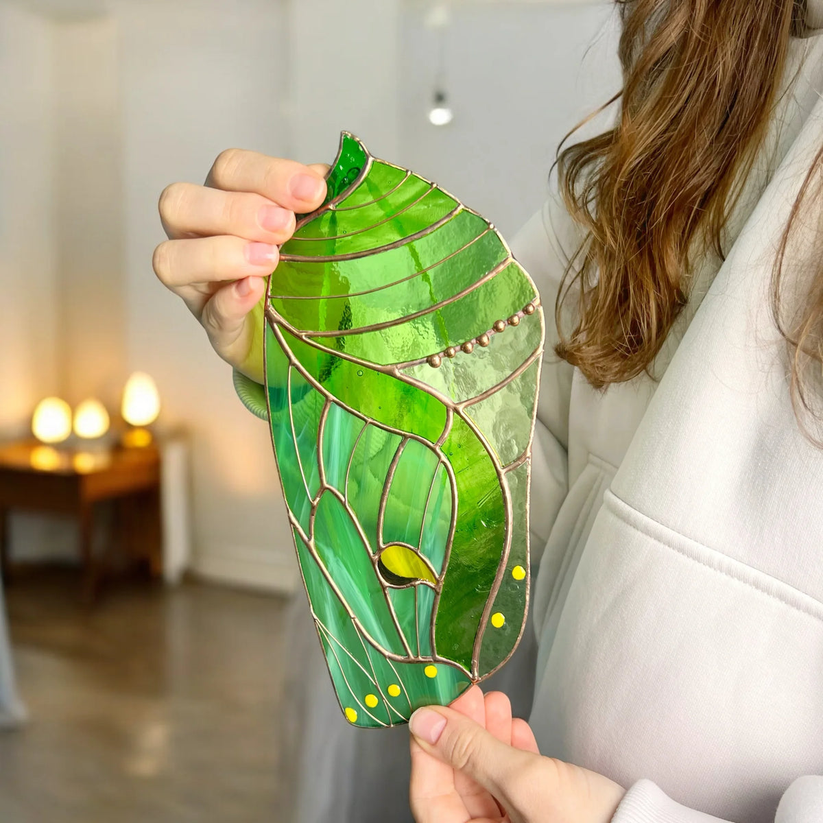 A person holding a beautiful green stained glass butterfly chrysalis indoors, making a wonderful and memorable gift for nature lovers.
