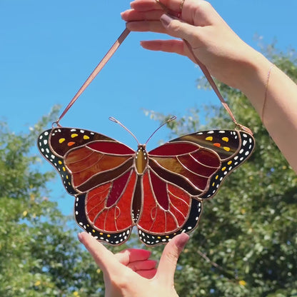 Video of stained glass monarch butterfly suncatcher being held in hands on front of garden view